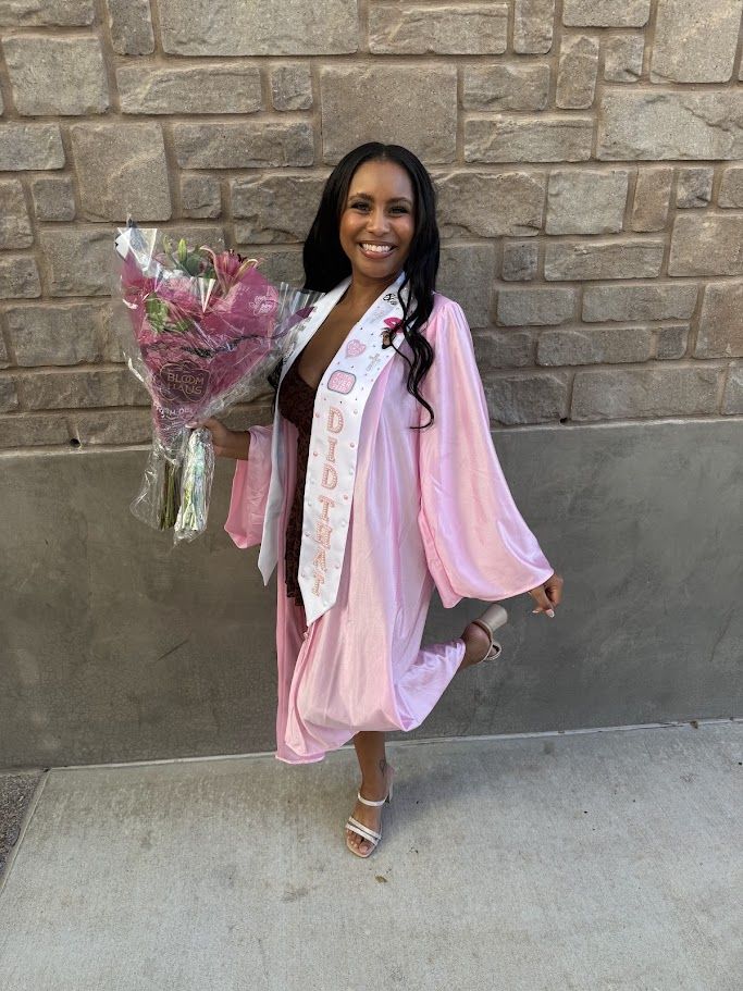 Nadia smiling at her Aveda Institute graduation, holding pink flowers